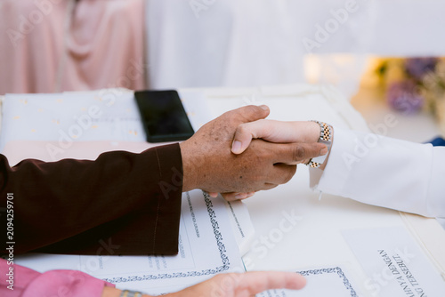 A meaningful close-up of the traditional handshake (Akad Nikah) between the groom and the marriage officiant during an Islamic solemnization ceremony.