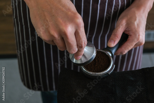 фотографія Barista coffee portafilter tamper hand apron ground bean preparation in cafe wit