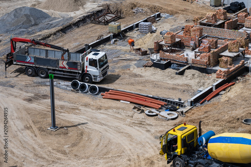Foto a white crane truck and a yellow concrete mixer parked near a new building foundation, where brickwork is underway alongside scattered pipes and building materials