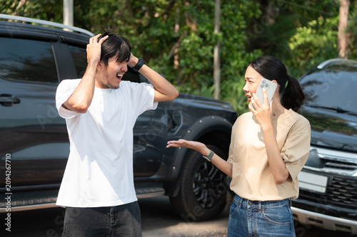 Two people involved in a roadside incident stand by the car, looking stressed as one calls for help after an unexpected problem.