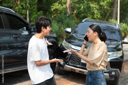 Two people involved in a roadside incident stand by the car, looking stressed as one calls for help after an unexpected problem.