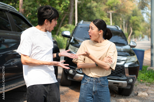 Two people involved in a roadside dispute argue beside their cars, showing shock and frustration after a sudden accident.
