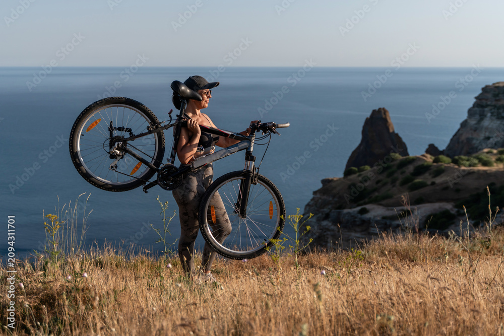 Fototapeta premium Cyclist bicycle athlete standing on a cliff edge overlooking the blue ocean during a beautiful sunny summer afternoon outdoors