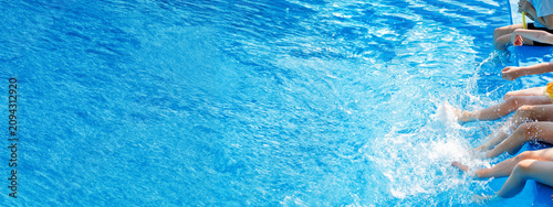 Happy children sitting by swimming pool and splashing water with legs