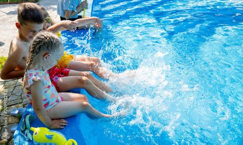 Happy children sitting by swimming pool and splashing water with legs