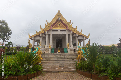 Fotografie Traditional Thai temple with a golden ornamented roof and grand entrance stairs flanked by golden statues and green plants