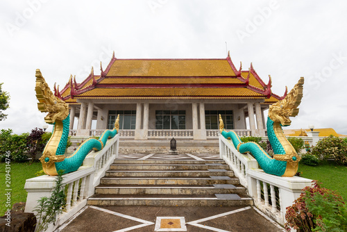 Fotografie Thai temple building featuring a traditional orange tiered roof and grand staircase flanked by ornate green and gold Naga serpent statues