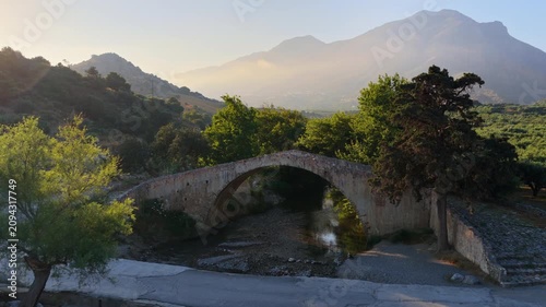 Aerial drone view of the old single-arch stone Preveli Bridge over a dry rocky riverbed among olive groves, Preveli, Greece