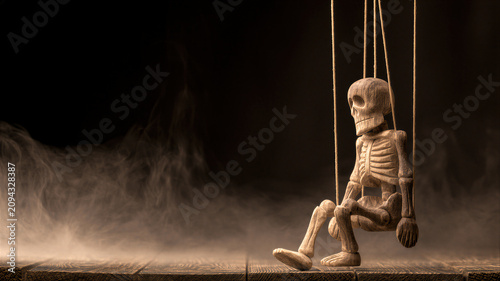 Wooden skeleton marionette hanging on strings in dark misty environment. Antique puppet concept for Halloween celebration. Scary doll character for horror story and mystic theater play.