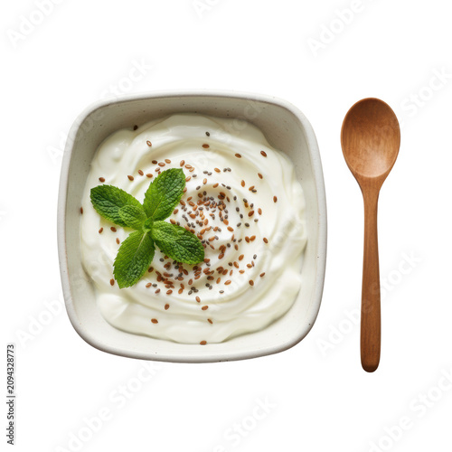 Handmade off-white ceramic bowl filled with thick creamy yogurt garnished with mint and seeds with a wooden spoon on white surface, wholesome nourishment concept