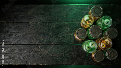 Glass jars with eyeballs in green liquid on dark wooden table. Spooky Halloween decoration with monsters eyes for holiday party. Scary laboratory experiment concept and spooky decor.