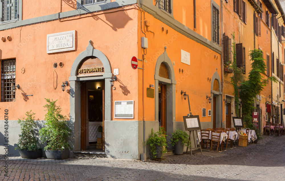 Obraz premium View of cobbled street with colorful old houses and cafe tables on a sunny morning in Trastevere, Rome, Italy.