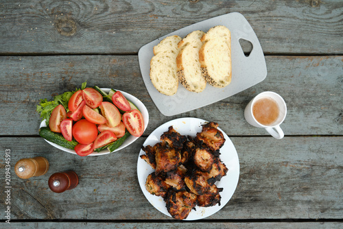Grilled chicken, fresh salad, and bread on wooden table during outdoor gathering