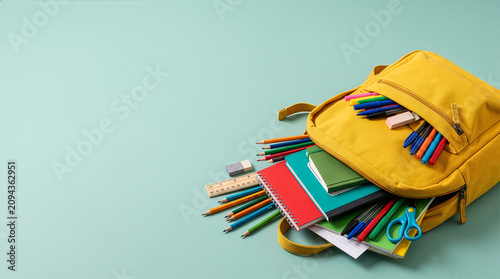 Yellow School Backpack Spilling Colorful Stationery and Notebooks on Mint Background with Copy Space