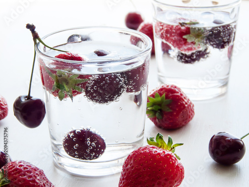 Принти на полотні Refreshing mineral water in glass with sweet cherries and strawberries, refreshing drink