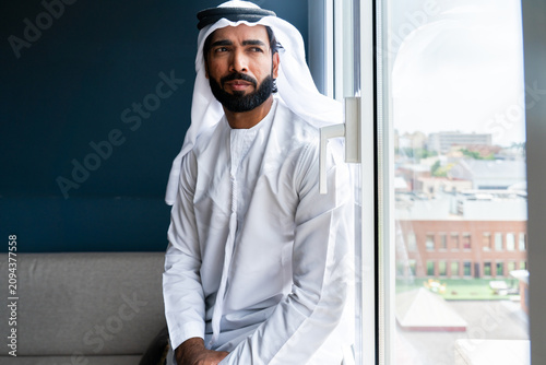 Foto Arab man looking out window wearing traditional kandura