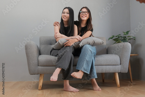 Happy Young Asian Female Friends Hugging Each Other While Sitting on a Sofa at Home