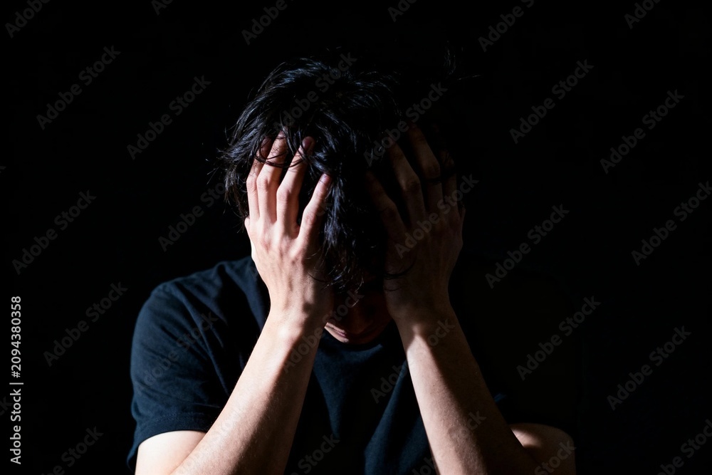 Fototapeta premium Stressed young man holding his head in darkness