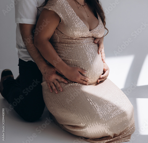 Side view of pregnant woman in sequin dress sitting on floor with husband hugging her belly