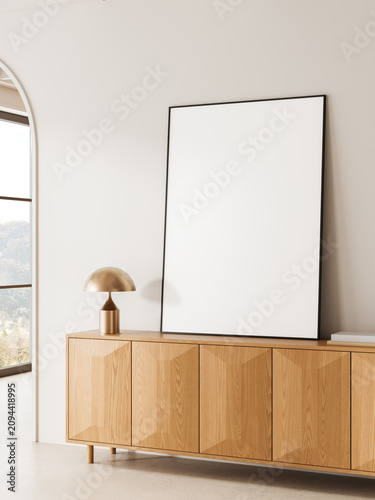 Minimal interior scene with large blank poster leaning on wooden cabinet beside modern lamp in bright room with soft daylight and clean design. 3D Rendering