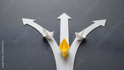 Leadership and unique business strategy concept showing a yellow paper boat taking a direct path while others diverge.