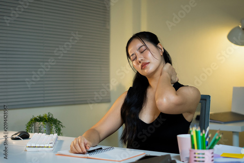 An Asian businesswoman rubs her painful neck due to office syndrome while working late at her desk.