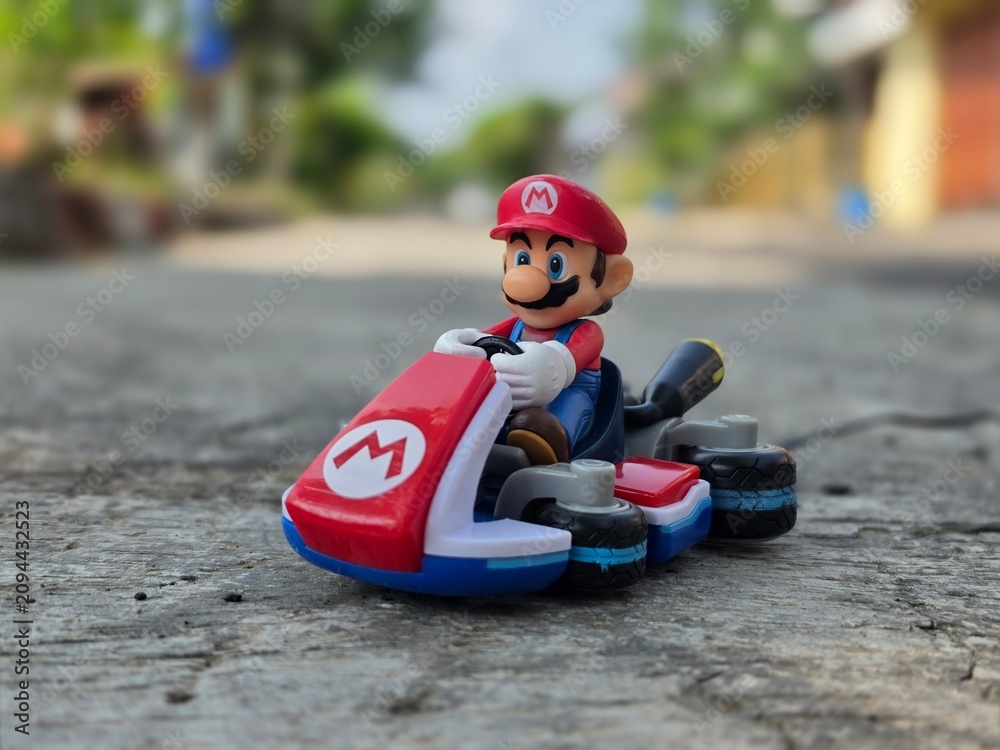 Obraz premium Indonesia - May 10, 2026 : Mini toy of action figure at outdoor with blurred background. Miniature photography concept design. Minifigure of Mario Bros character from Cartoon Gaming with his car.