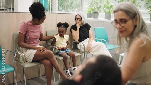 Diverse group of people sitting in a hospital waiting room. A man with spina bifida is in the foreground, talking with a woman