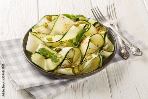 Zucchini Carpaccio is a raw courgettes salad with with pistachios, chili pepper and mint close-up in a plate on the table. Horizontal