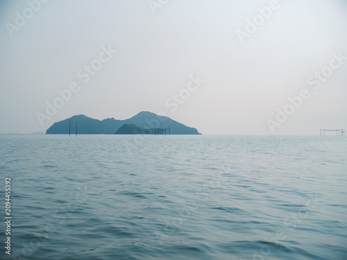 Serene ocean view of a distant green island against a hazy sky, calm natural background.
