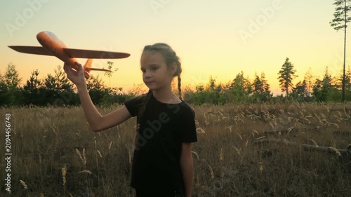 Child aviator with airplane dreams of traveling in summer in nature at sunset. Girl with plane on meadow. Summer leisure.