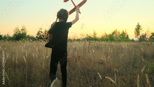 Girl play with toy airplane. Children toy plane in hands of child in summer in park under sun. Concept of child's dream of flying, child runs across field at sunset.
