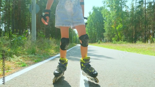 Child girl in casual clothes roller skating on road in forest on sunny summer day.