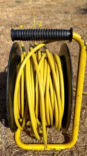 Vertical video social media - Closeup of the wound yellow cable or cord coils on a power extension reel, continuing to unravel on the rotating drum after pulling has stopped.