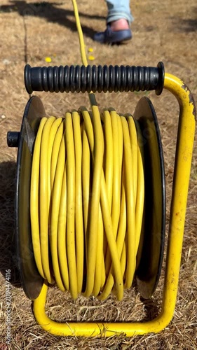 Vertical video social media - Closeup of a man’s hand pulling on a yellow cable or cord of a power extension reel, in a garden or yard, then walking away as the drum rotates.
