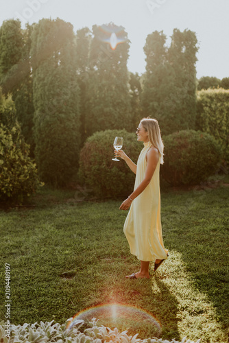 Woman in a yellow dress enjoys a drink while walking in a sunny garden