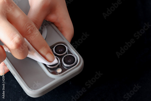Close-up of a woman's hand cleaning a smartphone camera lens with a microfiber cloth. Removing dust, fingerprints, and smudges for clear photos, device maintenance, and electronics care.