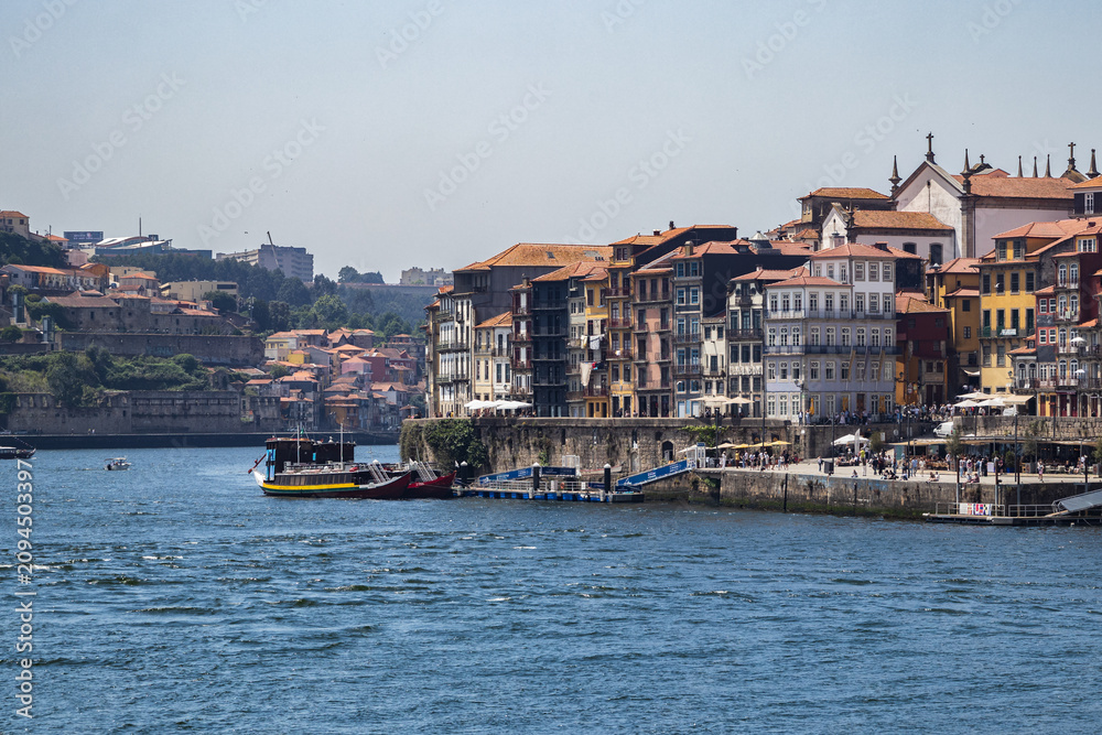 Obraz premium Vistas de la ribera de Oporto con sus edificios tradicionales de colores junto al rio Duero y barcos rabelos amarrados en el muelle en Portugal.