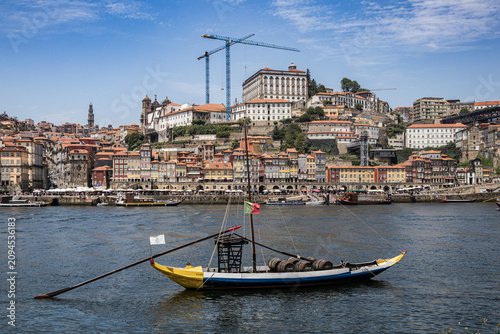 Foto Barco rabelo tradicional cargado con barriles de vino en el río Duero, con la pintoresca ribera de Oporto y el Palacio Episcopal de fondo, Portugal
