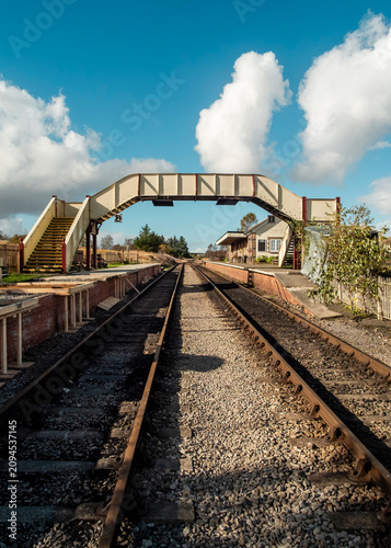 Bild auf Leinwand An empty heritage railway station with a traditional pedestrian footbridge spanning the tracks, reflecting a nostalgic and preserved setting for historic rail travel in the countryside