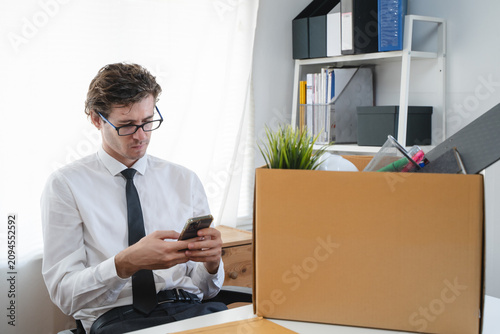 Obraz na plátně Young stressed businessman packing his belongings after being fired using smartp
