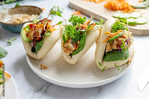 Gourmet teriyaki chicken bao buns garnished with sesame seeds on a ceramic plate.