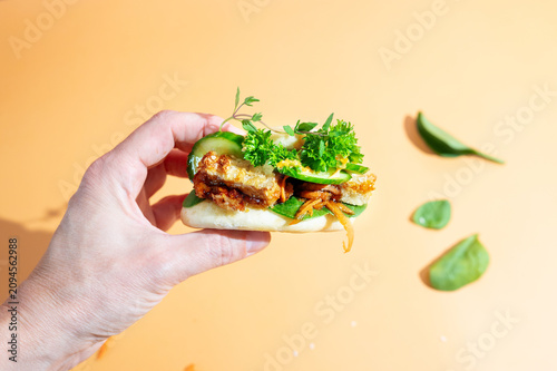 Close-up of a woman's hand holding a fluffy bao bun filled with tender chicken.
