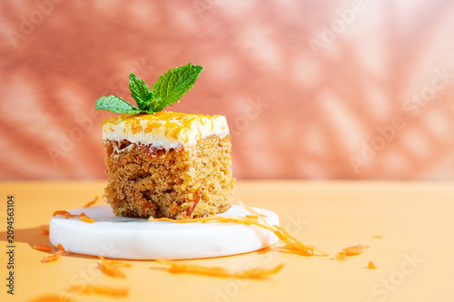 A slice of carrot cake served on a plate against a bright yellow background.