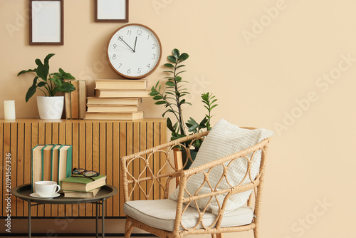 Quadro su tela Cozy living room interior with a wicker chair, books, plants, and a wall clock o