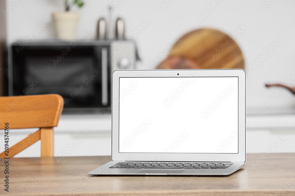 Fototapeta premium Laptop with blank white screen on a wooden kitchen table, home office and remote work