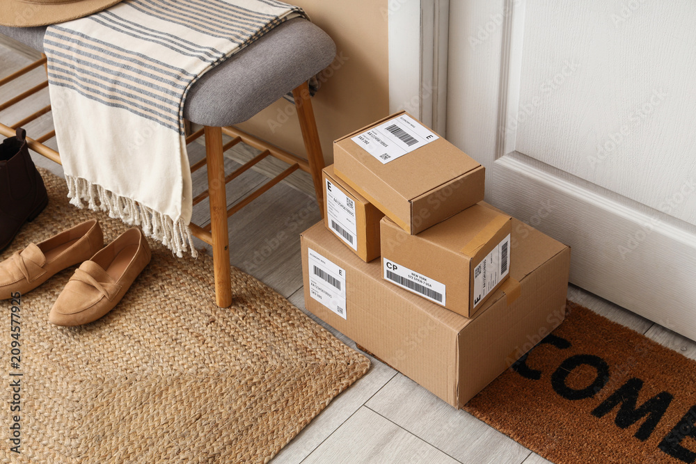 Obraz premium Stack of cardboard delivery boxes on a welcome mat at a residential front door, online shopping and shipping concept, Multiple packages with shipping labels are ready for pickup or recently