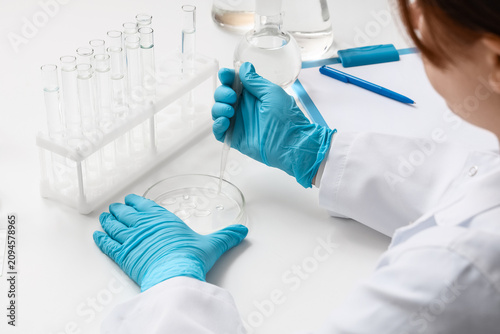 Female scientist dropping water sample onto Petri dish at table in laboratory...