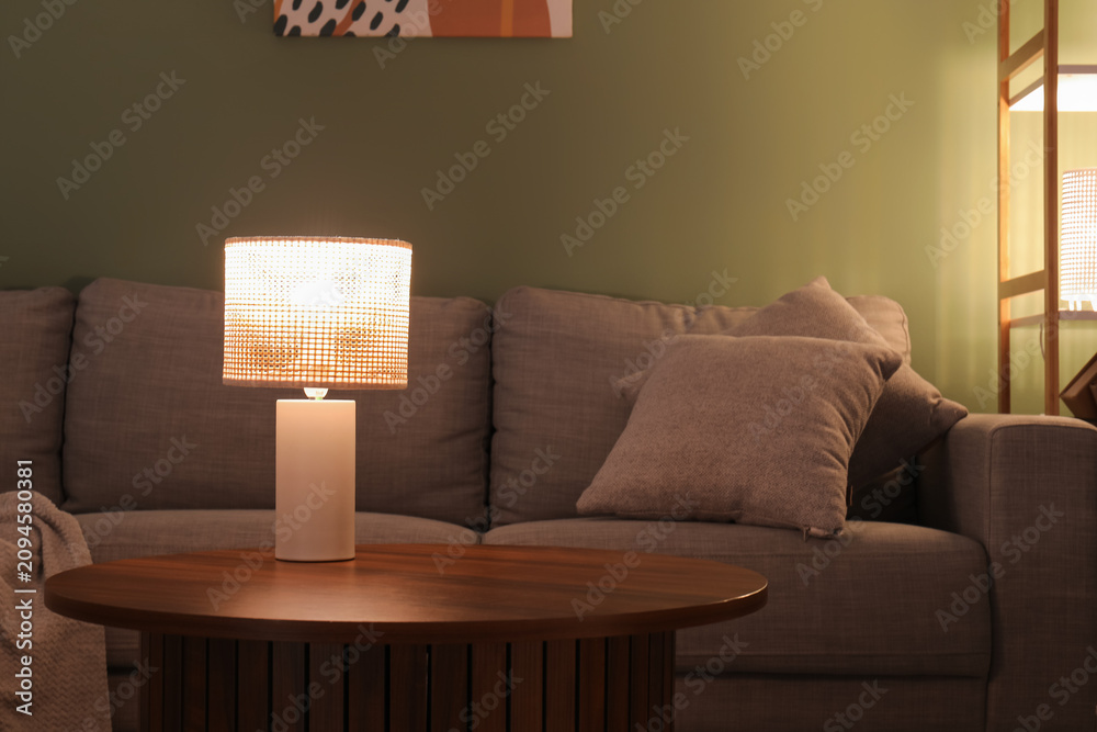 Obraz premium Glowing lamp on coffee table in dark living room at evening, closeup