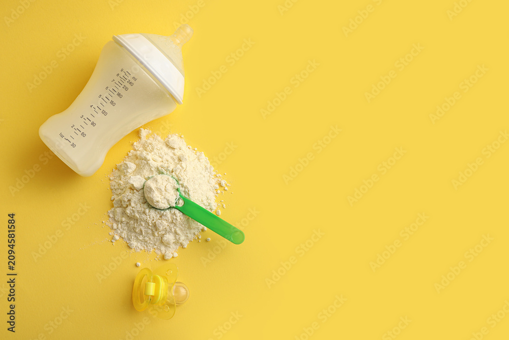 Obraz premium Scoop of powdered baby milk formula with bottle and pacifier on yellow background